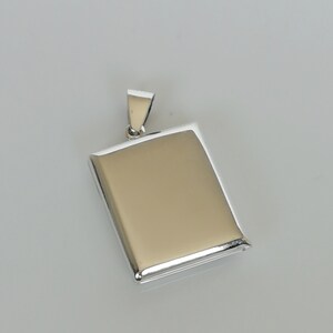 May include: A silver locket pendant with a rectangular shape and a hinged lid. The locket is smooth and shiny.