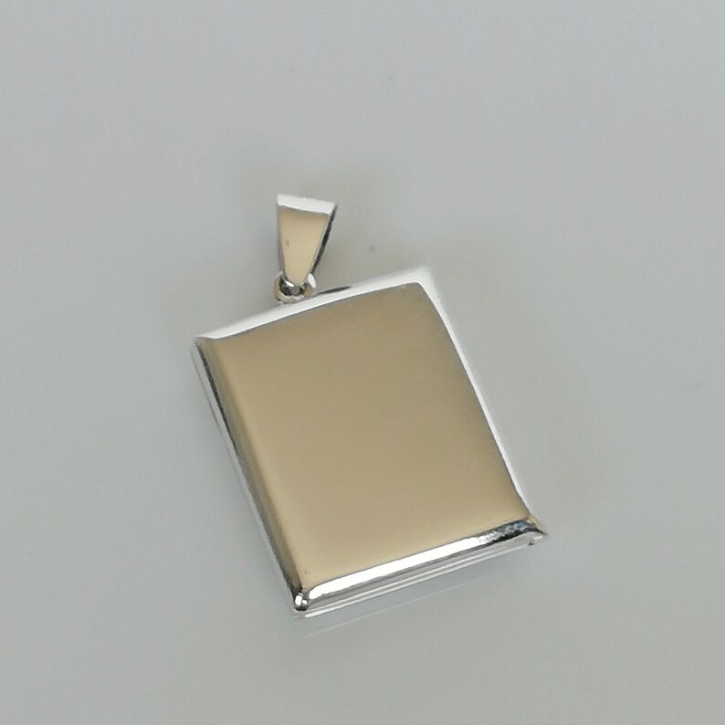 May include: A silver locket pendant with a rectangular shape and a hinged lid. The locket is smooth and shiny.
