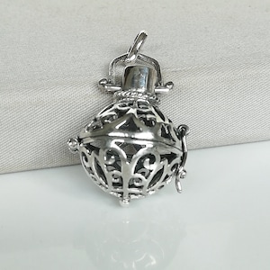 May include: A silver filigree cage pendant with a delicate design. The cage is open on one side and has a small loop at the top for attaching to a chain.