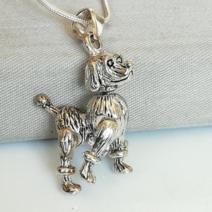Puede incluir: Collar con colgante de plata con un encanto de caniche detallado. El caniche está de pie sobre sus cuatro patas con la cola enroscada. El encanto es de plata y tiene un acabado texturizado.