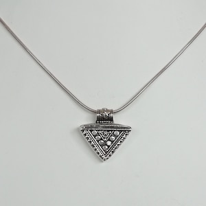 Puede incluir: Un collar de plata con un colgante triangular que presenta un diseño geométrico con pequeños círculos.