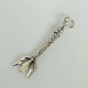 May include: Silver charm in the shape of a trident with an ornate design. The charm has a loop at the top for attaching to a necklace or bracelet.