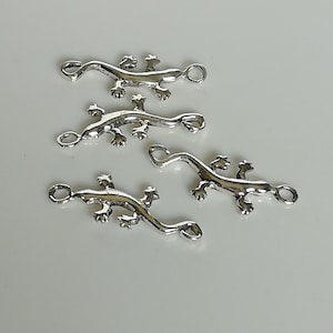 May include: Four silver-colored lizard charms. Each charm has a loop at the head and tail for attaching to jewelry. The lizards have detailed legs and a curved body.