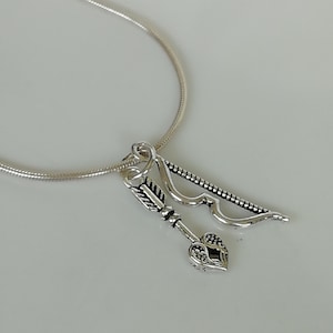 May include: A silver necklace with a charm featuring a silver arrow with a heart-shaped arrowhead and a silver bow.