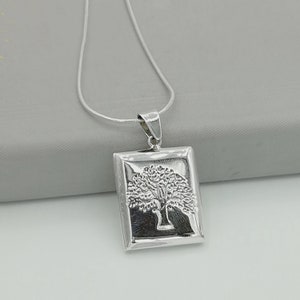 May include: A silver necklace with a rectangular pendant featuring a detailed tree design. The pendant is attached to a silver chain.