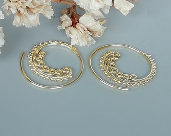 May include: A pair of gold hoop earrings with a decorative, swirling design. The earrings are made of metal and have a circular shape.