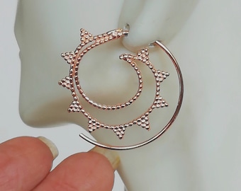 May include: Rose gold hoop earrings with a double layered design. The outer hoop is a simple circle, while the inner hoop features a repeating pattern of small triangles.
