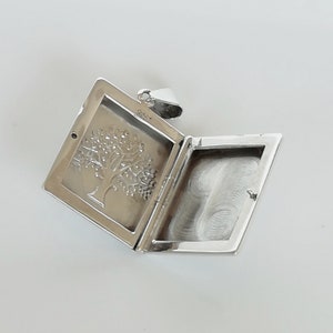 May include: Silver locket pendant with a tree design on the front and a blank space on the inside for a photo or message.