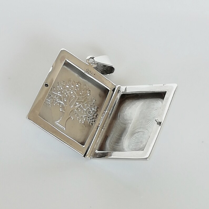 May include: Silver locket pendant with a tree design on the front and a blank space on the inside for a photo or message.