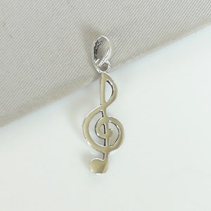 Puede incluir: Un colgante de plata en forma de clave de sol. El colgante es un recorte detallado de una clave de sol con una pequeña nota en la parte inferior.