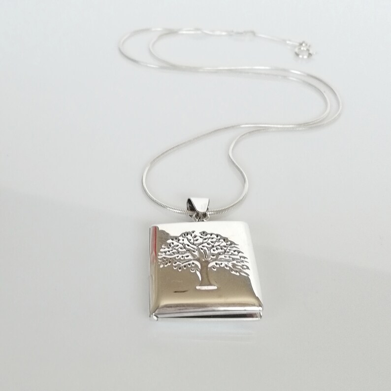 May include: A silver necklace with a square pendant featuring an etched tree of life design.