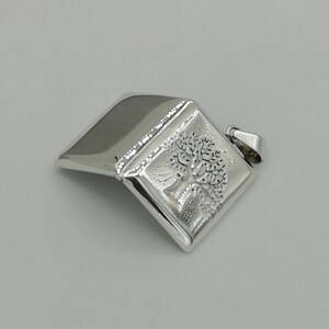 May include: A silver pendant in the shape of a closed book with a tree design engraved on the front.