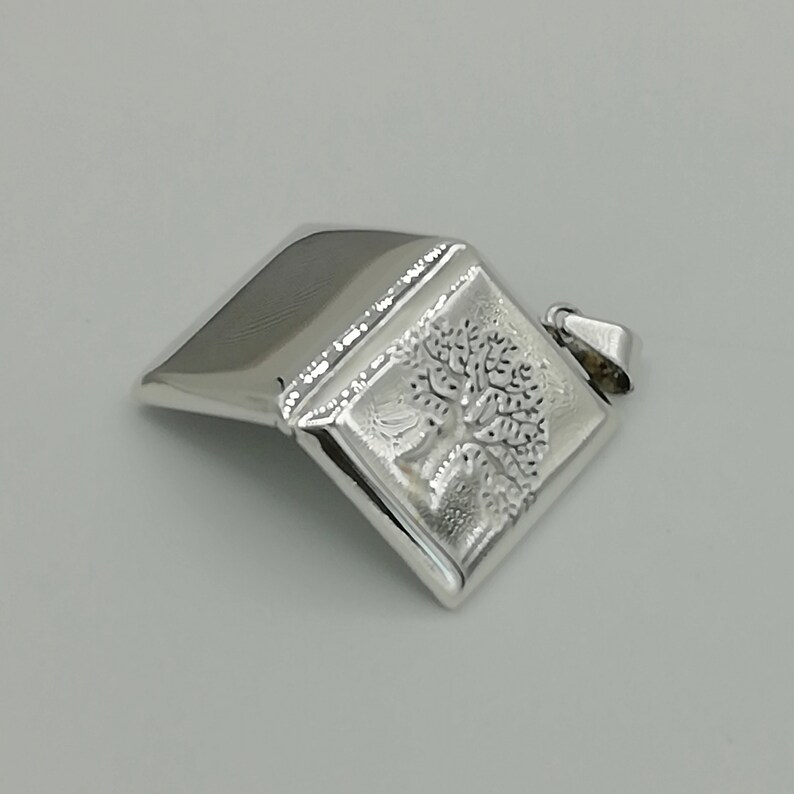 May include: A silver pendant in the shape of a closed book with a tree design engraved on the front.