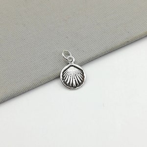 May include: A silver seashell charm pendant. The charm is round and features a detailed seashell design.