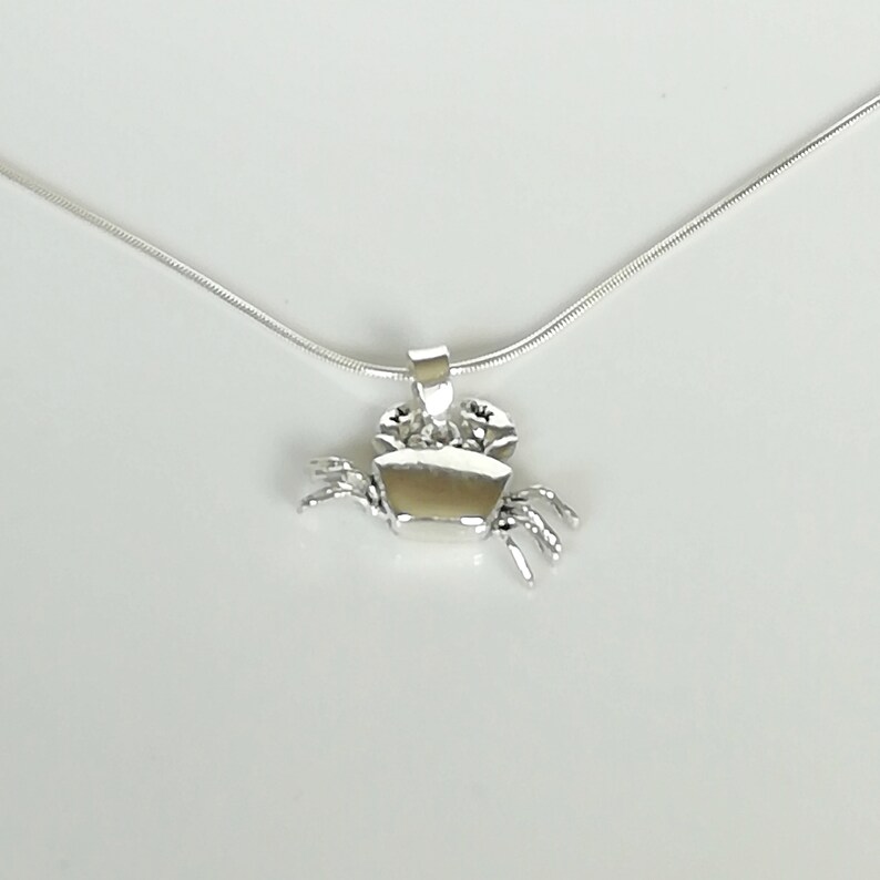 May include: A silver crab pendant on a delicate silver chain. The crab pendant is detailed with claws, eyes, and a textured shell. The necklace is displayed against a white background, highlighting the jewelry's design.