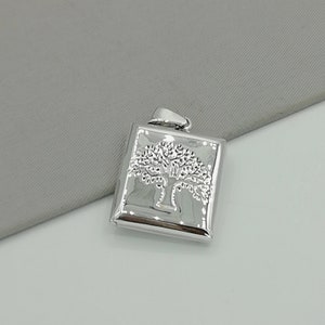 May include: Silver pendant featuring a tree of life design. The pendant is square shaped and has a textured surface.