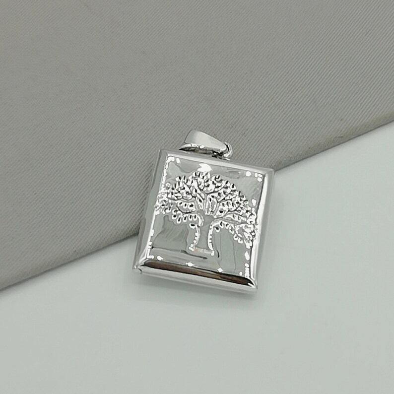 May include: Silver pendant featuring a tree of life design. The pendant is square shaped and has a textured surface.