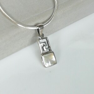 May include: A silver chain necklace with a pendant featuring a white mother-of-pearl square stone set in a silver frame with a geometric design.