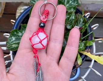 May include: A red and white macrame keychain with a clear crystal stone, black bead, and silver feather charms.
