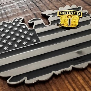 May include: A black and silver metal American flag shaped like an eagle with a gold "Retired" patch on the eagle's chest.