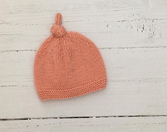 May include: A peach-coloured knitted baby hat with a knotted top.