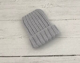 May include: A grey knitted beanie hat with a ribbed texture. The hat is folded down at the brim.