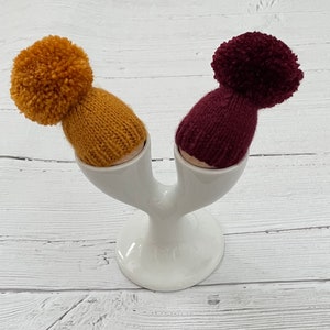 Set of two knitted hand knitted egg cosies-burgundy and gold