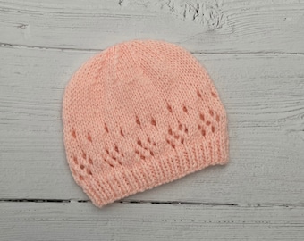 May include: A pink knitted hat with a lacy pattern. The hat is made of soft yarn and has a comfortable fit.