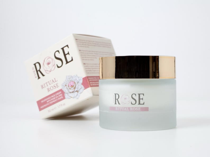 May include: A frosted glass jar of Ritual Rose nourishing face cream with a metallic gold lid, accompanied by its matching white cardboard box. The packaging features the text Ritual Rose, a rose illustration, and the volume 50 ml 1.7 fl oz.