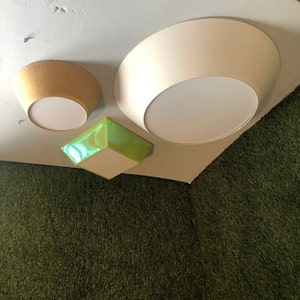Puede incluir: Tres lámparas de techo, una blanca, una verde y una beige, están montadas en un techo blanco sobre un fondo verde.