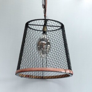 Puede incluir: Una lámpara colgante de jaula de metal negro con una correa de cuero marrón. La luz tiene una bombilla de vidrio transparente en el interior.