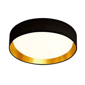 May include: A round black ceiling light fitting with a gold trim. The light fitting has a fabric shade.