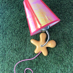 May include: A pink and yellow iridescent lampshade with a yellow star-shaped base and a pink cord.