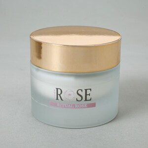May include: A cylindrical glass jar with a frosted finish and a shiny gold lid. The front of the jar features the text "EDEN ROSE" in black lettering with a rose graphic replacing the letter "O", and the text "RITUAL ROSE" on a pink bar below.