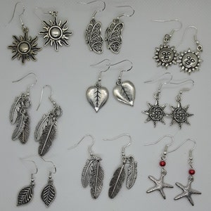May include: A collection of 12 silver earrings featuring various designs, including suns, leaves, hearts, and stars. The earrings are all made of metal and have a silver finish.