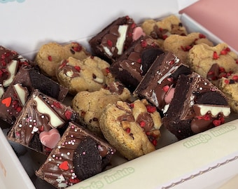 Puede incluir: Una caja llena de una variedad de productos horneados, que incluyen brownies y galletas. Los brownies están decorados con varios ingredientes, como chocolate, chispas y caramelos en forma de corazón. Las galletas son doradas y tienen varios ingredientes.