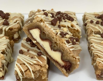 Op de afbeelding: Close-up van een stapel chocoladekoekjes met witte chocolade drizzle en chocolade chips. De repen zijn in vierkanten gesneden en hebben een witte chocolade vulling.