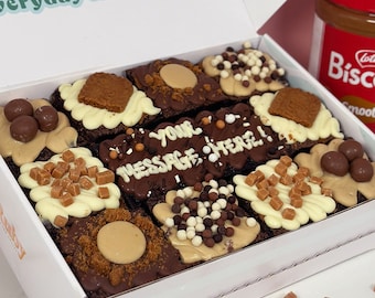 May include: A white box filled with nine different decorated brownies. Each brownie has a different topping, including chocolate, caramel, and white chocolate. The box is open and the brownies are visible. The text "everyday is cake day..." is printed on the top of the box.