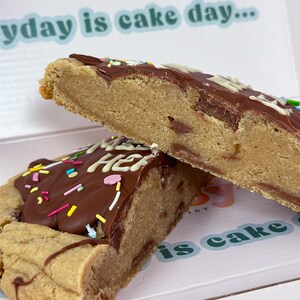 May include: Two chocolate chip cookie slices topped with chocolate frosting and colorful sprinkles. The top slice has the words "Happy Birthday" written in white frosting. The bottom slice has the words "Today is cake day..." written in green.
