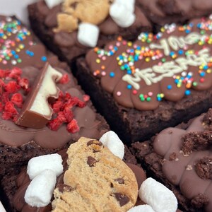May include: Assortment of chocolate brownies with various toppings, including sprinkles, chocolate chips, cookie pieces, marshmallows, and chocolate pieces. One brownie has the words "You Mess" written in white chocolate.