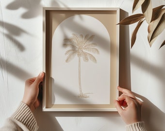Puede incluir: Una impresión enmarcada de una palmera con un fondo beige y un arco blanco. La impresión está en un marco de madera claro.