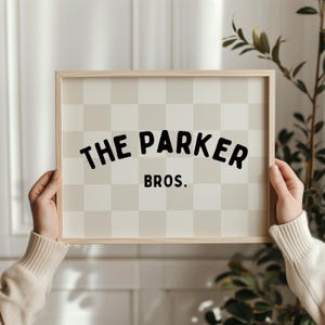 May include: A wooden framed sign with a checkered background. The sign says "The Parker Bros." in black text.
