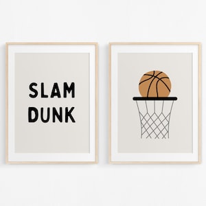 Peut inclure: Deux impressions encadrées sur le thème du basketball. La première impression affiche les mots "SLAM DUNK" en texte noir sur un fond beige. La deuxième impression montre un ballon de basket brun passant à travers un panier noir avec un filet gris sur un fond beige.