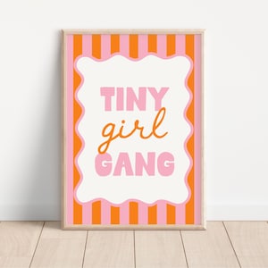 Può includere: Una stampa artistica incorniciata con le parole "TINY girl GANG" in lettere rosa e arancioni. Lo sfondo presenta strisce verticali rosa e arancioni. L'opera d'arte è in una cornice di legno chiaro.