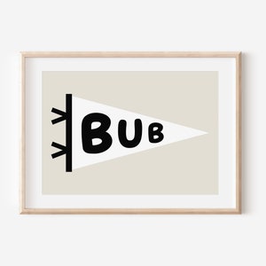 May include: A white pennant with black trim and the word "BUB" in black block letters. The pennant is on a beige background and is framed in a light wood frame.