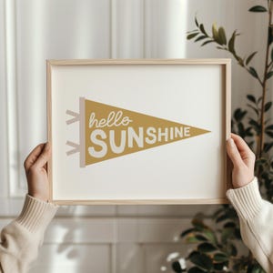 Może przedstawiać: Wydruk w ramie z żółtym wzorem chorągiewki z napisem "hello sunshine" w białym kolorze.