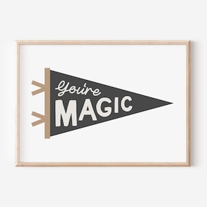 May include: A framed print featuring a pennant design with the words "You're MAGIC" in white lettering on a dark gray background. The pennant is attached to a tan-colored wooden frame, set against a white background.