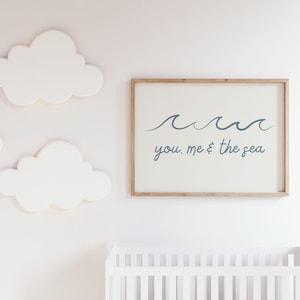 Könnte beinhalten: Ein weißer gerahmter Druck mit einem blauen Wellendesign und dem Text "you, me & the sea". Der Druck hängt an einer weißen Wand mit drei weißen wolkenförmigen Dekorationen.