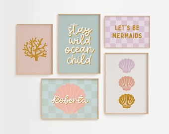 May include: Set of six framed prints with a beach theme. The prints feature a coral, seashells, and text that says "stay wild ocean child" and "let's be mermaids". One print has a seashell with the name "Roberta" on it.