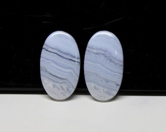 May include: Two oval-shaped blue lace agate stones. The stones have a light blue base color with darker blue and gray banding patterns. The polished stones are smooth and have a glossy finish. These stones are suitable for jewelry making or collecting.